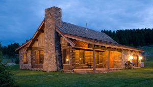 forest service cabin at dusk with warm lights on inside and stone and logs exterior