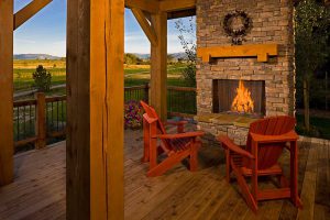 outdoor fireplace on deck with wooden chairs and golden and green fields in the background