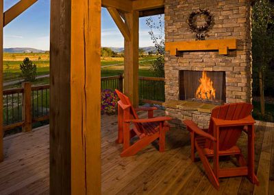 outdoor fireplace on deck with wooden chairs and golden and green fields in the background