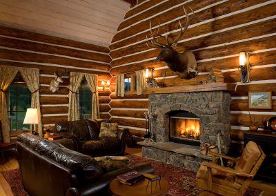 log home interior living space with couches surrounding a stone fireplace and mounts