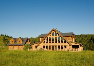 flat view of log home with sloped ceilings and picture windows nestled in forest with secondary development
